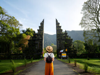 Traveler wanita dengan ransel menikmati pintu masuk pura Hindu Bali