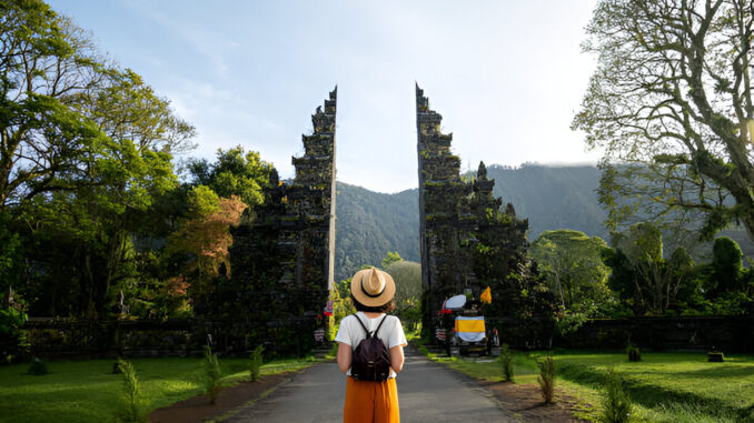 Traveler wanita dengan ransel menikmati pintu masuk pura Hindu Bali